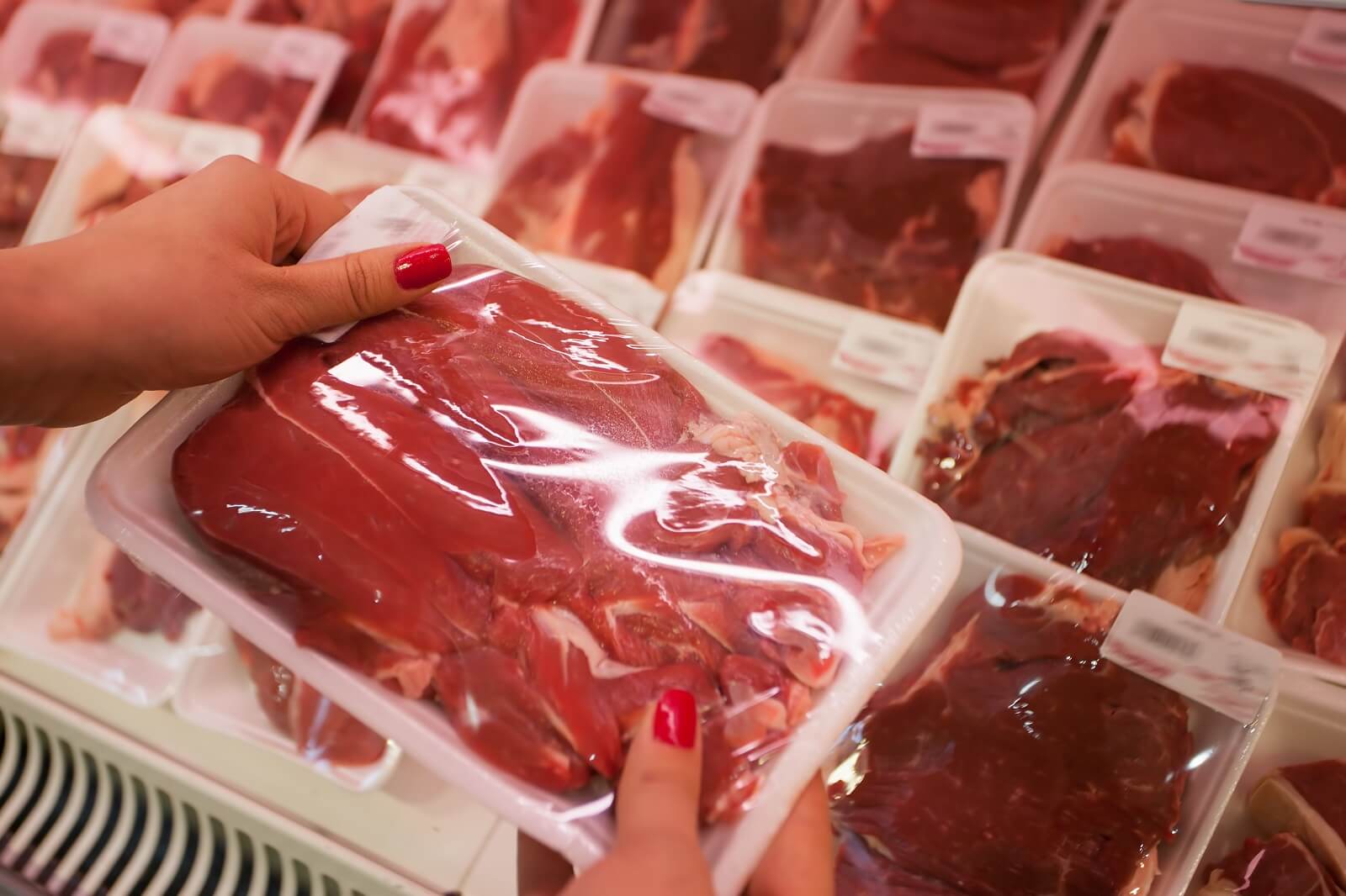 woman with red nails holds shrink wrapped raw meat
